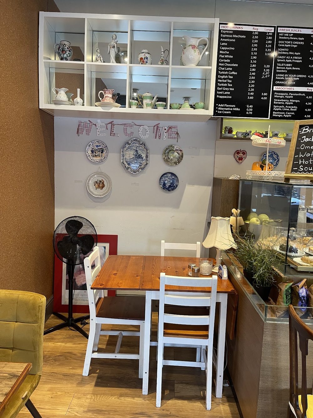A quiet corner of the cafe with a small wooden table, white chairs and shelves of china ornaments