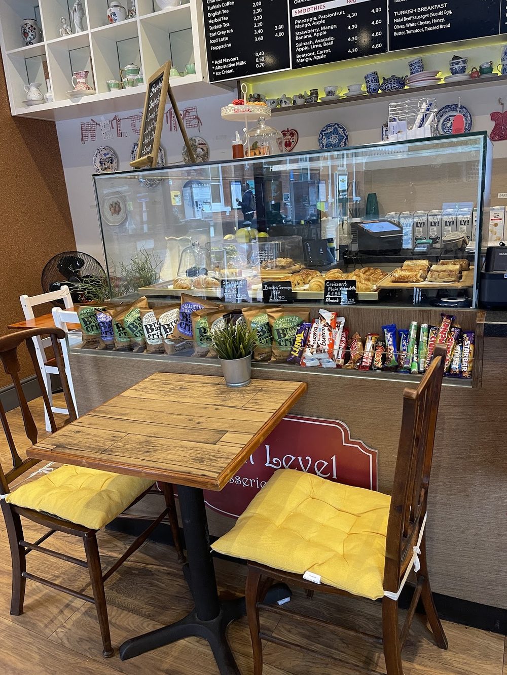 A wooden table with yellow-cushioned chairs in front of the pastry counter